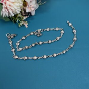 Delicate silver heart-link anklet arranged on a blue background with floral accents