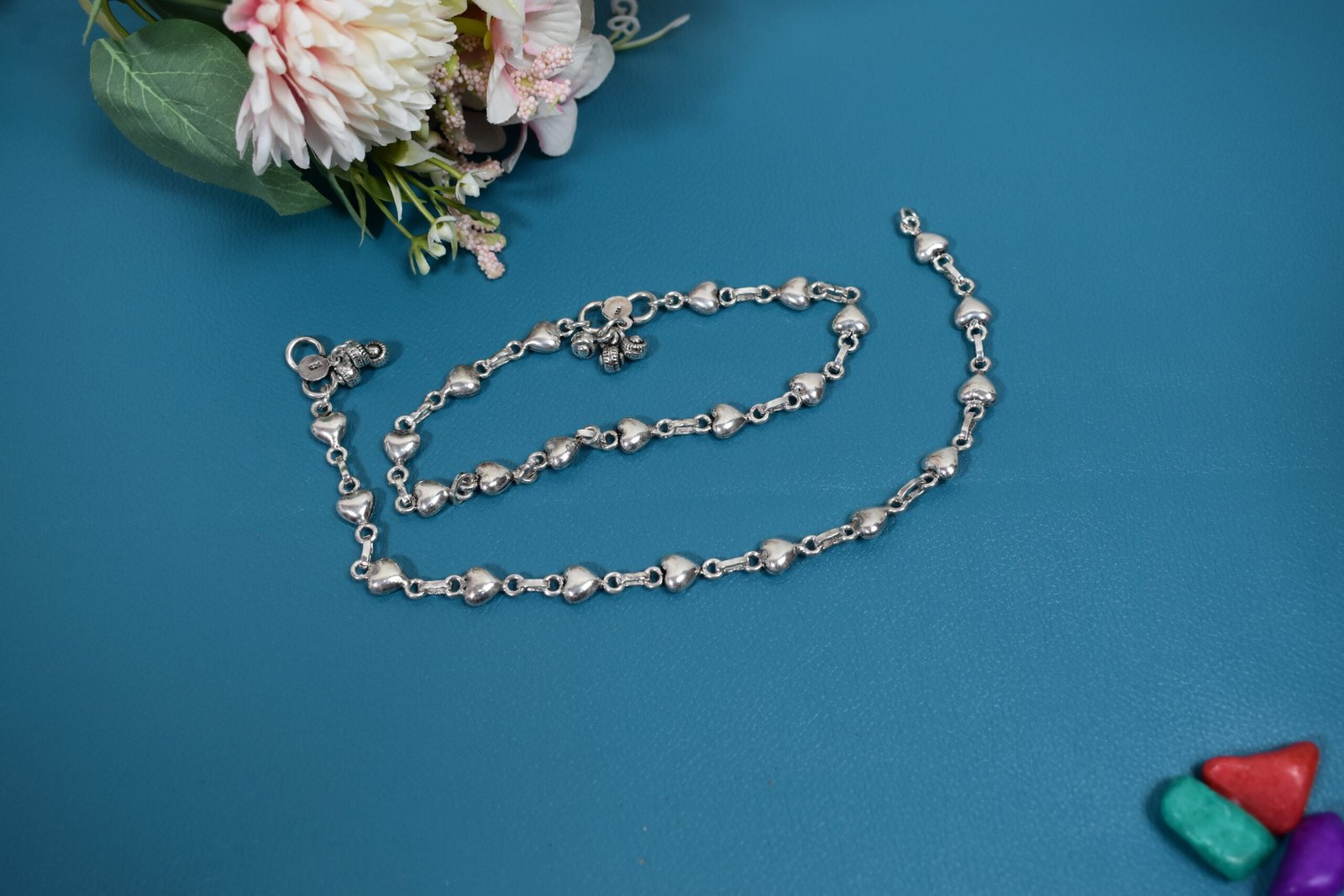 Silver Heart Link Anklet | Sukhambika 925 Atelier Delicate silver heart-link anklet arranged on a blue background with floral accents