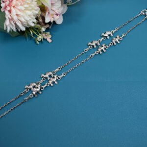 Pair of Sukhambika 925 sterling silver anklets with multiple detailed elephant charms linked on a fine chain, resting on a textured teal background with floral and decorative accents