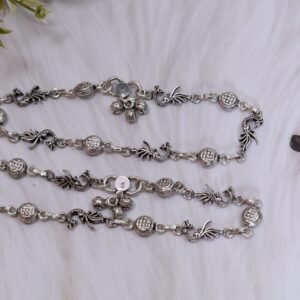 Sterling silver anklets featuring alternating oxidized peacock links and textured round discs, laid parallel on a plush white faux fur surface, highlighting the ghungroo bell clusters near the clasps.
