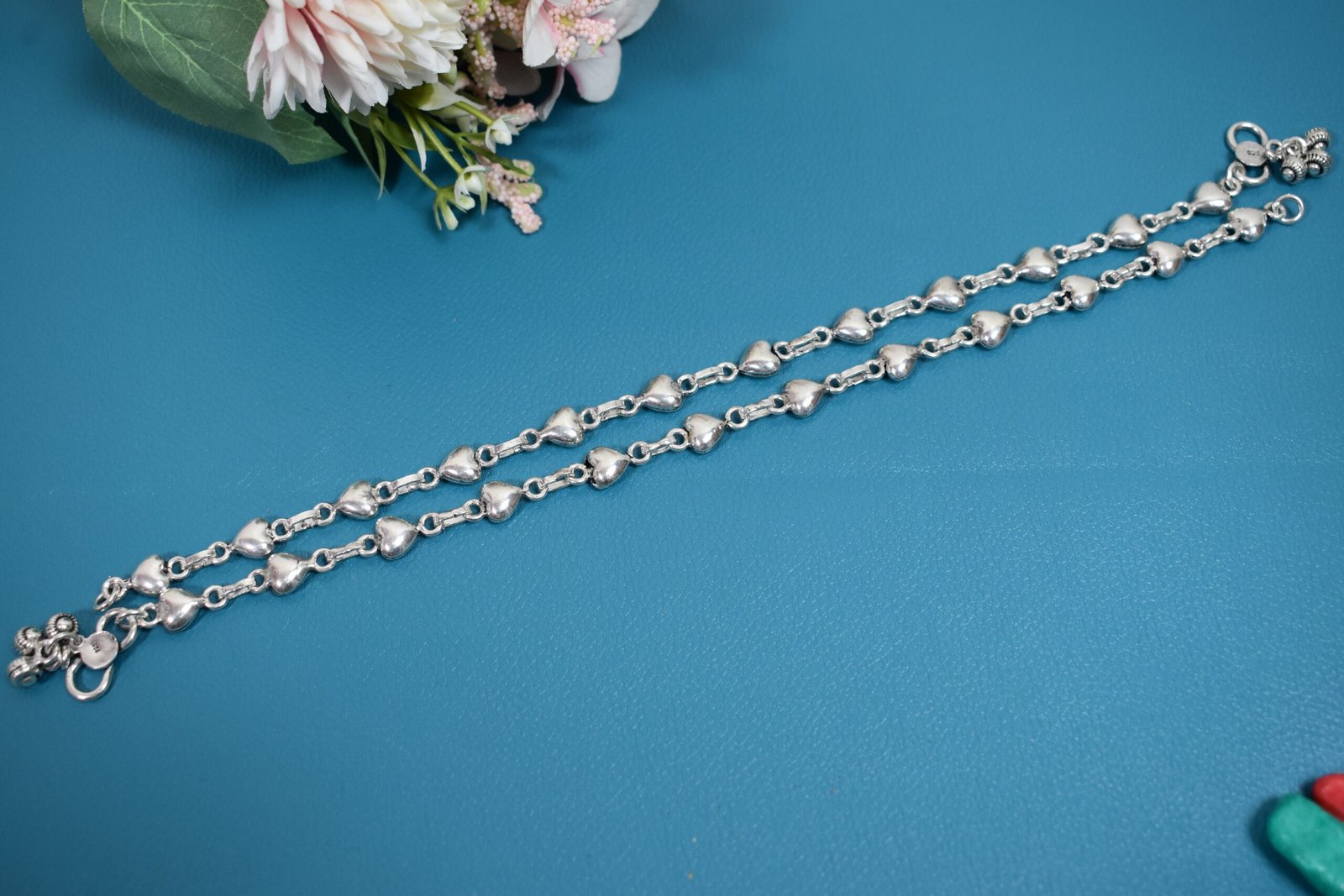 Silver Heart Link Anklet | Sukhambika 925 Atelier Delicate silver heart-link anklet arranged on a blue background with floral accents