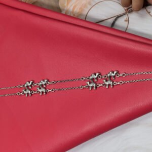 Pair of Sukhambika 925 sterling silver anklets with multiple detailed elephant charms linked on a fine chain, resting on a textured teal background with floral and decorative accents