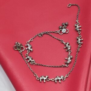 Pair of Sukhambika 925 sterling silver anklets with multiple detailed elephant charms linked on a fine chain, resting on a textured teal background with floral and decorative accents
