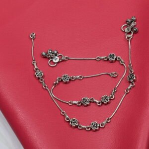 Close-up of a single 925 sterling silver anklet featuring detailed oxidized rose links and a cluster of larger, textured ghungroo bells on a smooth snake chain, resting on red textured leather. A clear '925' stamp is visible near the clasp