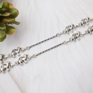 Pair of Sukhambika 925 sterling silver anklets with multiple detailed elephant charms linked on a fine chain, resting on a textured teal background with floral and decorative accents