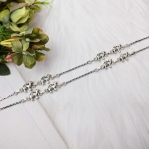 Pair of Sukhambika 925 sterling silver anklets with multiple detailed elephant charms linked on a fine chain, resting on a textured teal background with floral and decorative accents