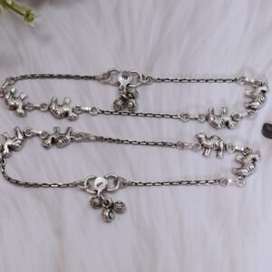 Pair of Sukhambika 925 sterling silver anklets with multiple detailed elephant charms linked on a fine chain, resting on a textured teal background with floral and decorative accents