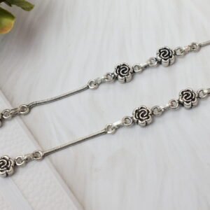Macro photograph showing a close-up of multiple oxidized rose flower links on a sterling silver chain, with a distinct '925' purity stamp near a smooth spherical clasp element against a clean white background.