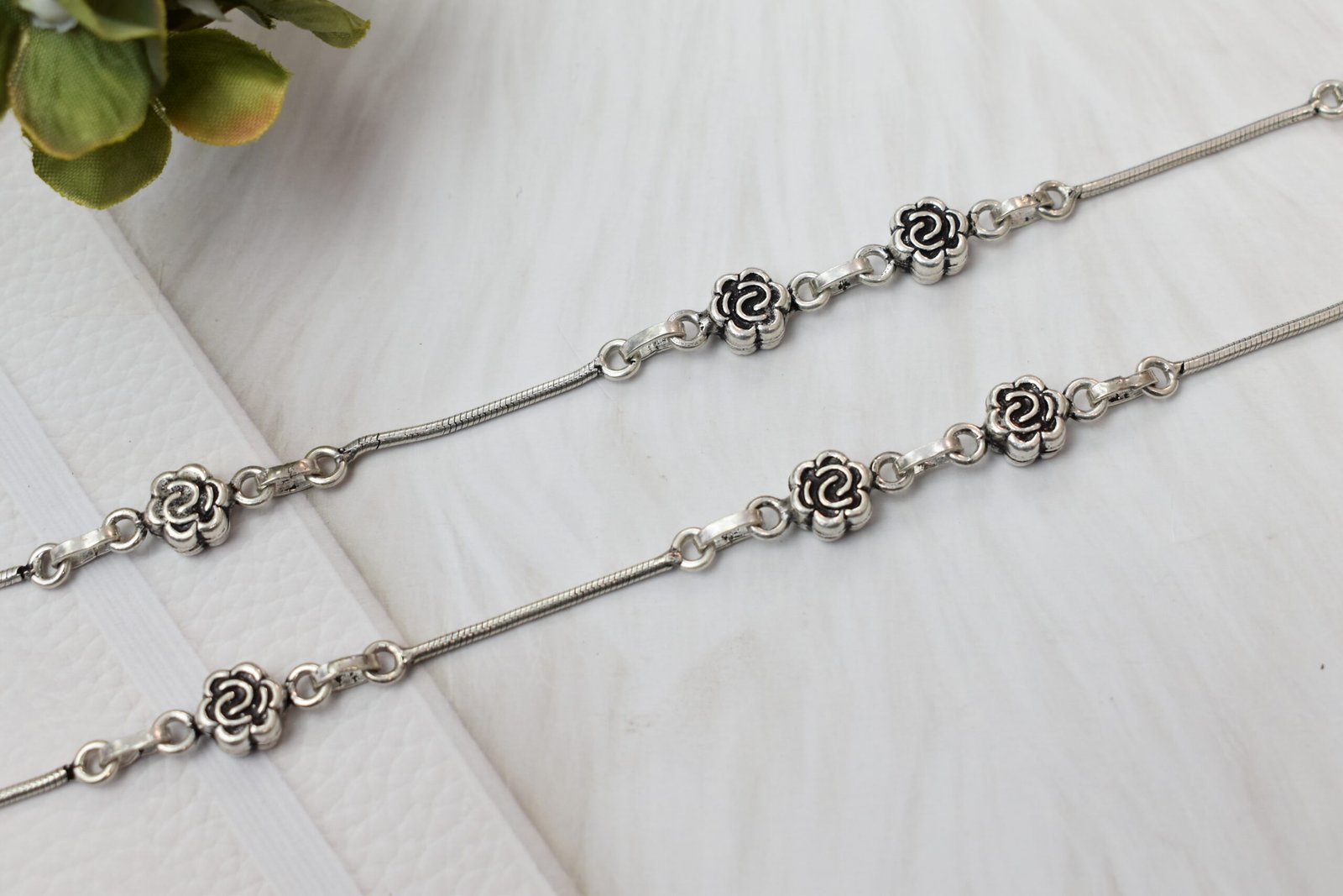 Micro-Focus-Multiple-Rose-Links-925-Stamp-Silver-Anklet-Sukhambika-925 Macro photograph showing a close-up of multiple oxidized rose flower links on a sterling silver chain, with a distinct '925' purity stamp near a smooth spherical clasp element against a clean white background.