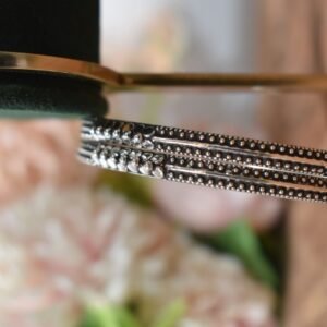A pair of 925 sterling silver kadas overlapping on a dark green velvet jewelry stand, showcasing an intricate barik dana (fine bead) pattern along the oxidized bands.