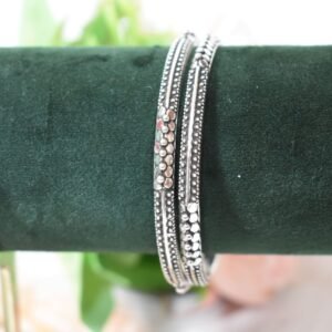 A pair of 925 sterling silver kadas overlapping on a dark green velvet jewelry stand, showcasing an intricate barik dana (fine bead) pattern along the oxidized bands.