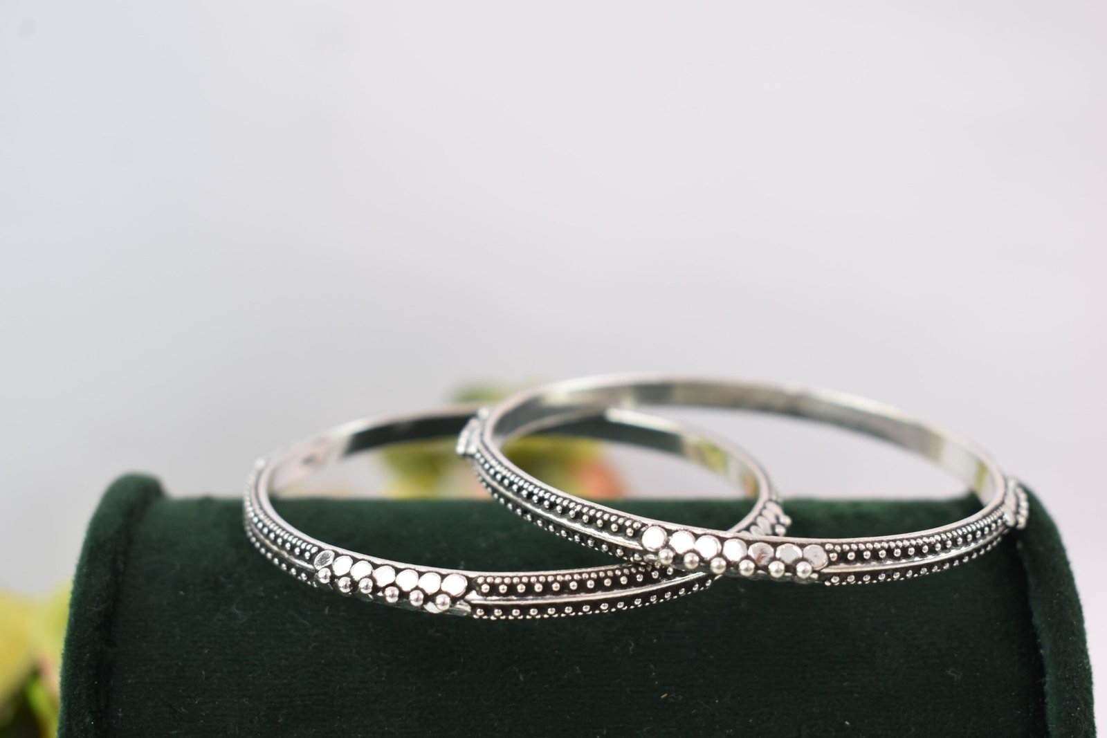 barik-dana-intricate-silver-kada3 A pair of 925 sterling silver kadas overlapping on a dark green velvet jewelry stand, showcasing an intricate barik dana (fine bead) pattern along the oxidized bands.