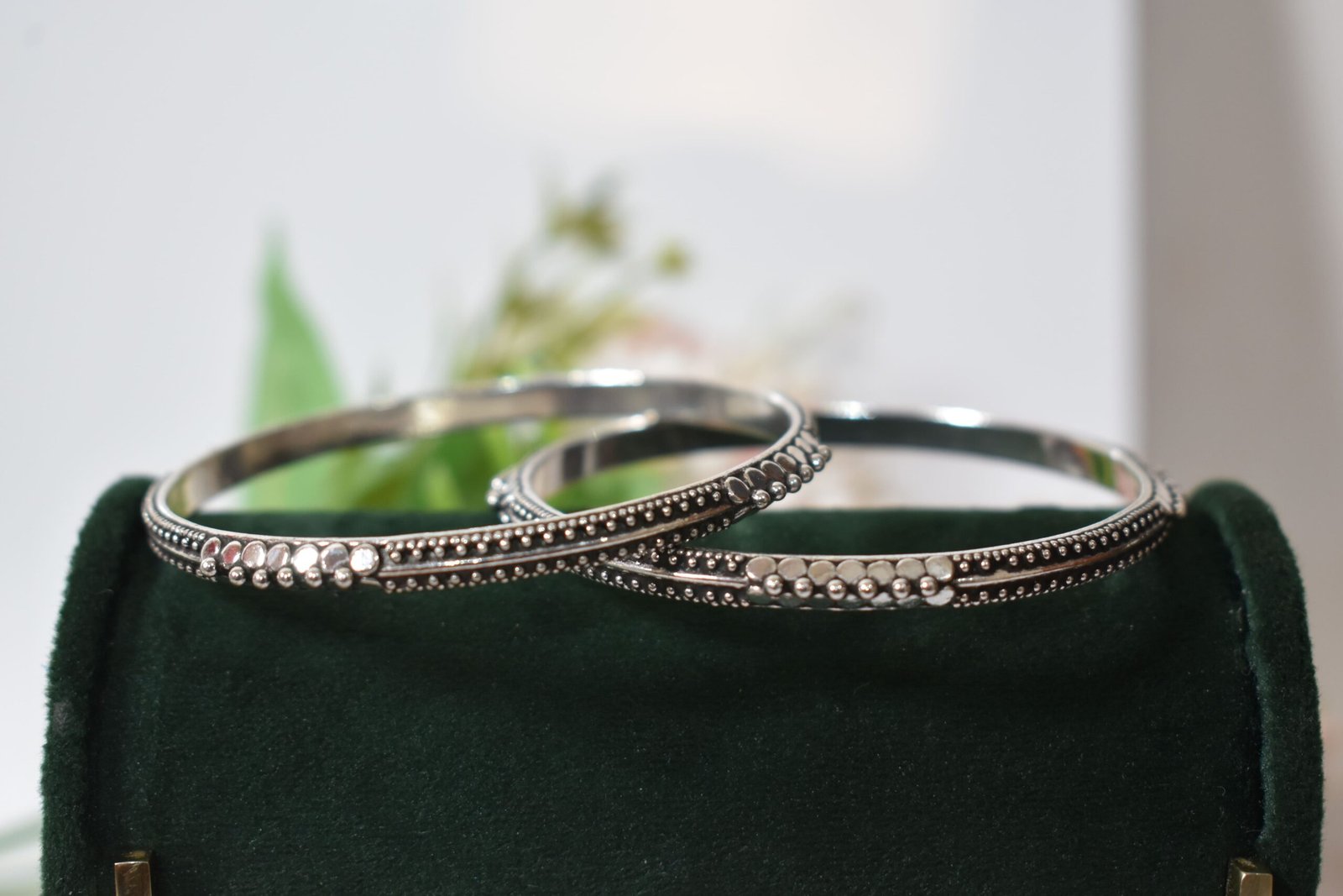 barik-dana-intricate-silver-kada4 A pair of 925 sterling silver kadas overlapping on a dark green velvet jewelry stand, showcasing an intricate barik dana (fine bead) pattern along the oxidized bands.