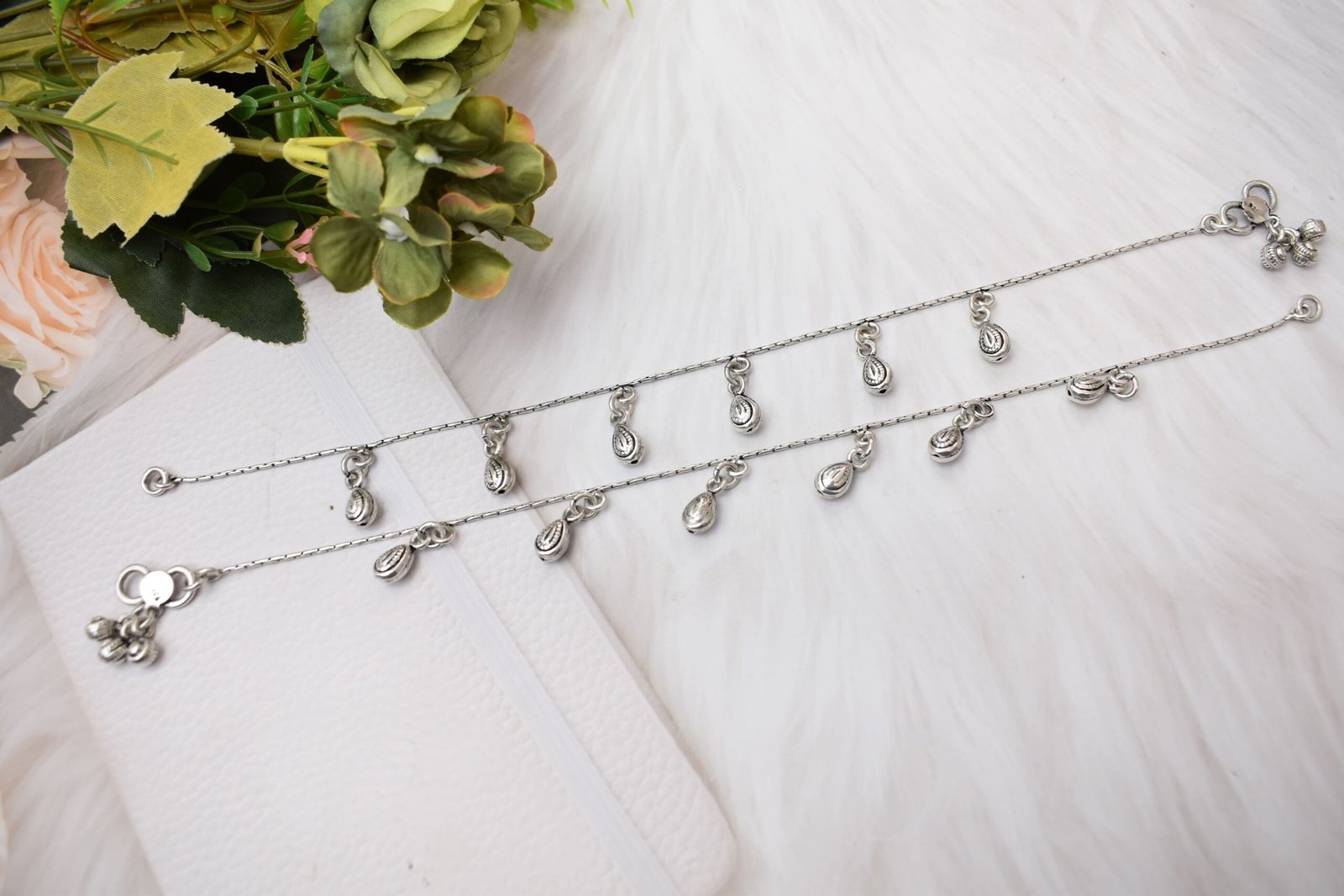 classic-chained-beads-drop-silver-anklets7 Two classic chained beads drop silver anklets resting on a white faux fur surface, showcasing the teardrop charms, an S-hook clasp with a 925 stamp, and tiny ghungroo bells