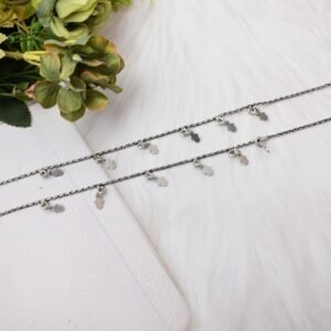 a pair of classic chained leaf shape drop 925 sterling silver anklets stretched across a white textured surface and white faux fur, featuring flat leaf charms and ghungroo bell clasps next to floral accents.