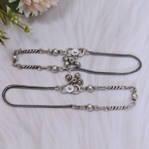 925 sterling silver anklets stretched across a white textured surface and soft faux fur, featuring a dual design with a smooth rope chain transitioning into a sequence of silver balls and twisted links, finished with a ghungroo clasp.