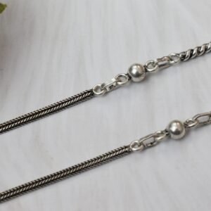 925 sterling silver anklets stretched across a white textured surface and soft faux fur, featuring a dual design with a smooth rope chain transitioning into a sequence of silver balls and twisted links, finished with a ghungroo clasp.