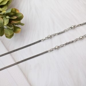 925 sterling silver anklets stretched across a white textured surface and soft faux fur, featuring a dual design with a smooth rope chain transitioning into a sequence of silver balls and twisted links, finished with a ghungroo clasp.
