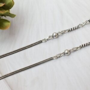 925 sterling silver anklets stretched across a white textured surface and soft faux fur, featuring a dual design with a smooth rope chain transitioning into a sequence of silver balls and twisted links, finished with a ghungroo clasp.