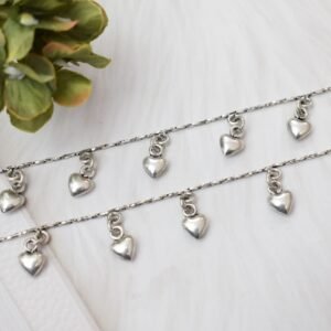 Detailed diagonal view of two silver chains featuring dangling heart-shaped beads, highlighting the twisted texture of the main chain against a soft white background.