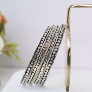 Four thin 925 sterling silver bangles overlapping on a soft white surface, displaying a continuous sequence of raised heart motifs framed by a textured, oxidized border.