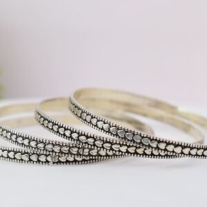 Four thin 925 sterling silver bangles overlapping on a soft white surface, displaying a continuous sequence of raised heart motifs framed by a textured, oxidized border.