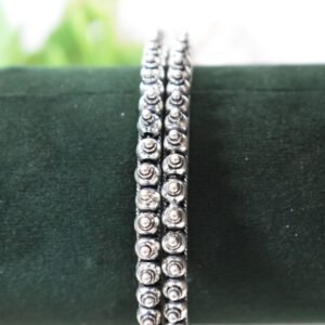 A pair of overlapping 925 sterling silver kadas resting on a soft white surface, showcasing a highly textured design that fuses larger polished silver balls with a smaller beaded edge against a dark, oxidized background.