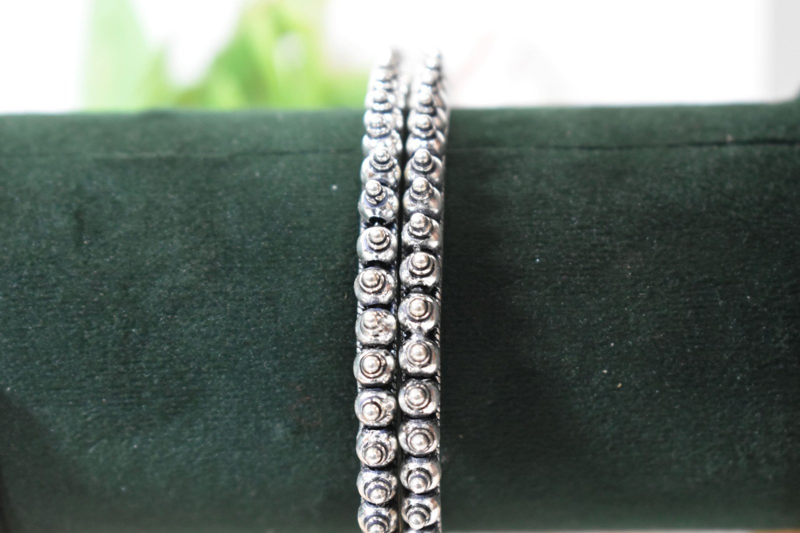 intricate-double-ball-fusion-everyday-wear-silver-kada2 A pair of overlapping 925 sterling silver kadas resting on a soft white surface, showcasing a highly textured design that fuses larger polished silver balls with a smaller beaded edge against a dark, oxidized background.