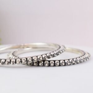 A pair of overlapping 925 sterling silver kadas resting on a soft white surface, showcasing a highly textured design that fuses larger polished silver balls with a smaller beaded edge against a dark, oxidized background.