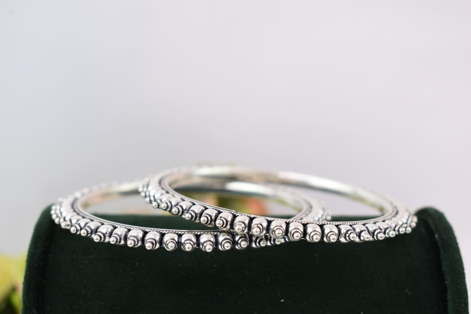 intricate-double-ball-fusion-everyday-wear-silver-kada5 A pair of overlapping 925 sterling silver kadas resting on a soft white surface, showcasing a highly textured design that fuses larger polished silver balls with a smaller beaded edge against a dark, oxidized background.