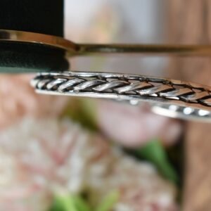 A 925 sterling silver kada featuring a traditional twisted rope or rassa design, resting horizontally on a dark green velvet jewelry stand against a soft white background.