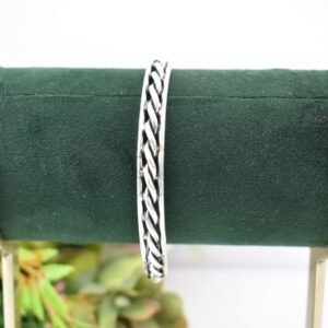 A 925 sterling silver kada featuring a traditional twisted rope or rassa design, resting horizontally on a dark green velvet jewelry stand against a soft white background.