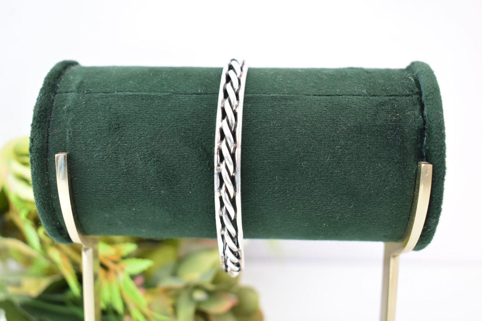rassa-design-everyday-wear-silver-kada2 A 925 sterling silver kada featuring a traditional twisted rope or rassa design, resting horizontally on a dark green velvet jewelry stand against a soft white background.