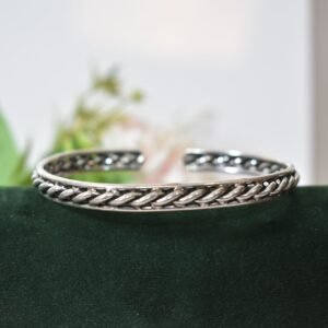 A 925 sterling silver kada featuring a traditional twisted rope or rassa design, resting horizontally on a dark green velvet jewelry stand against a soft white background.