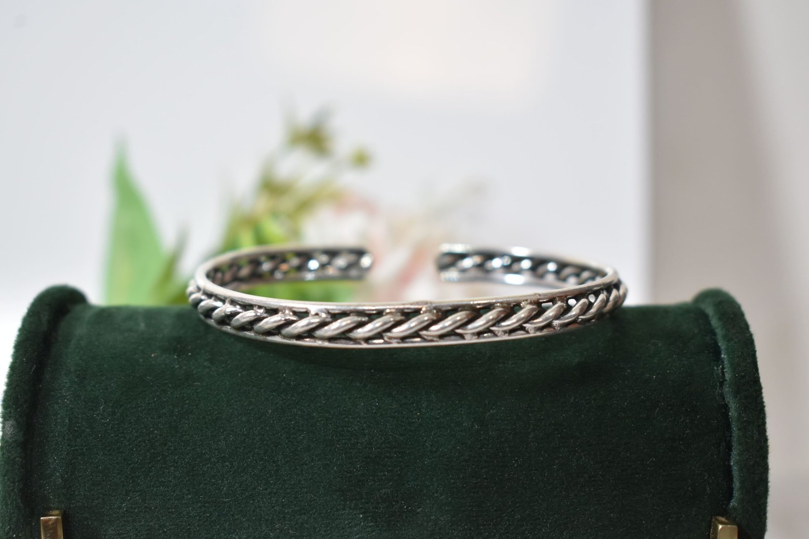 rassa-design-everyday-wear-silver-kada3 A 925 sterling silver kada featuring a traditional twisted rope or rassa design, resting horizontally on a dark green velvet jewelry stand against a soft white background.