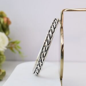 A 925 sterling silver kada featuring a traditional twisted rope or rassa design, resting horizontally on a dark green velvet jewelry stand against a soft white background.