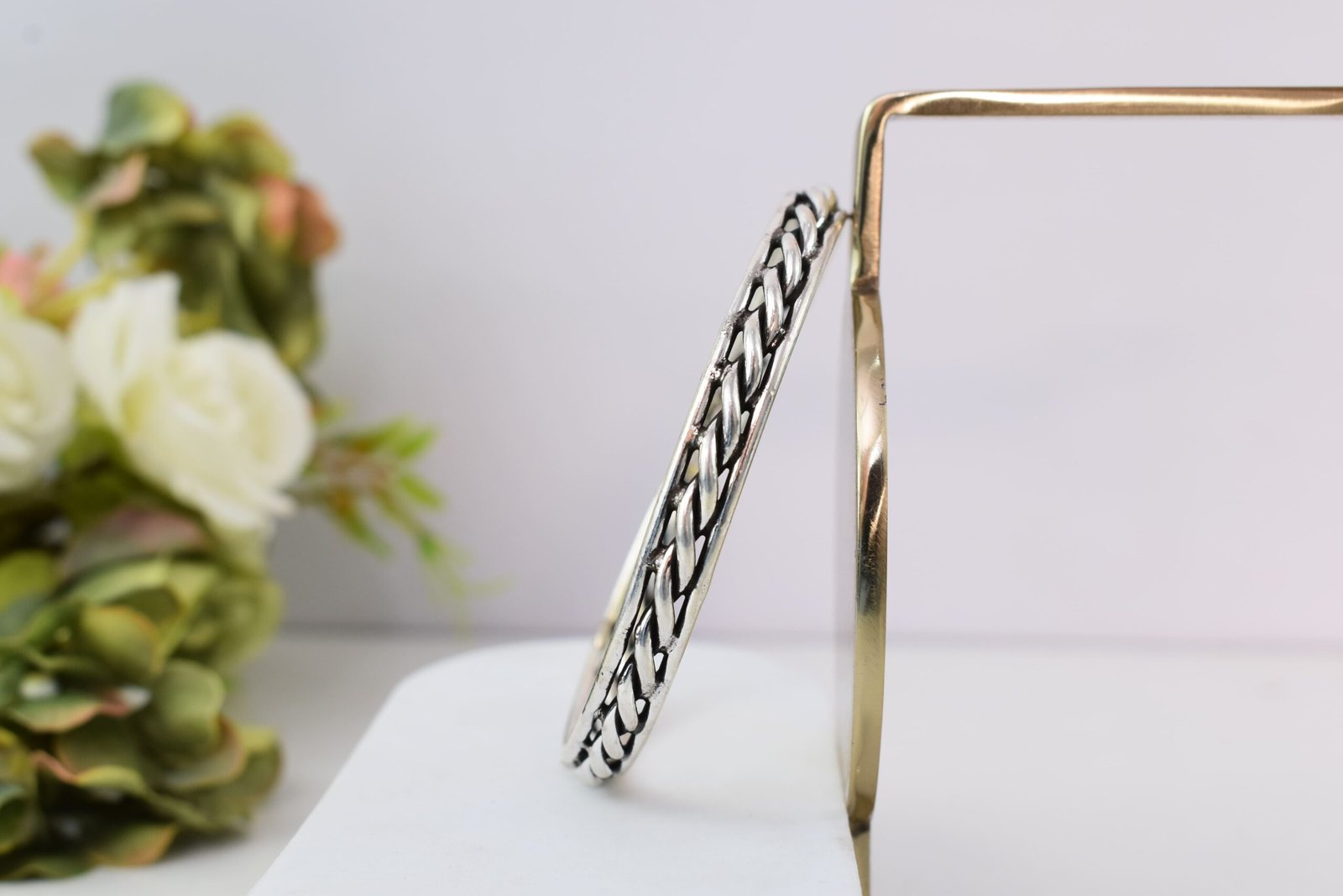 rassa-design-everyday-wear-silver-kada4 A 925 sterling silver kada featuring a traditional twisted rope or rassa design, resting horizontally on a dark green velvet jewelry stand against a soft white background.