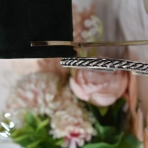 A 925 sterling silver kada featuring a traditional twisted rope or rassa design, resting horizontally on a dark green velvet jewelry stand against a soft white background.