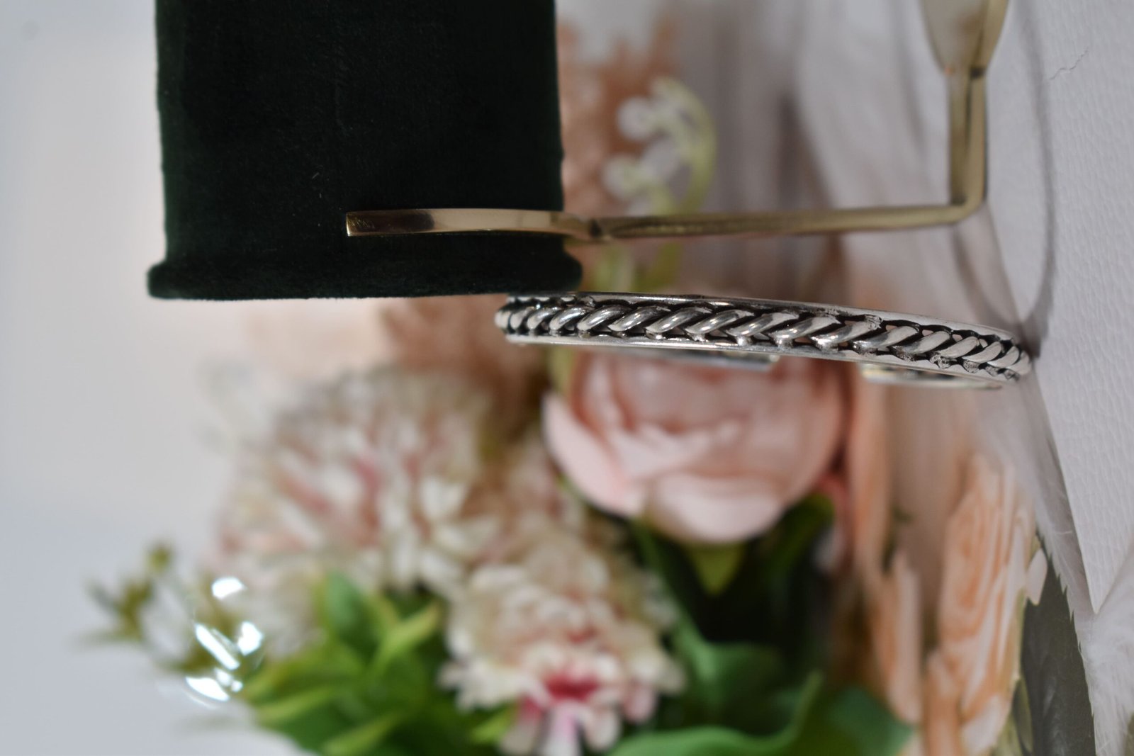 rassa-design-everyday-wear-silver-kada5 A 925 sterling silver kada featuring a traditional twisted rope or rassa design, resting horizontally on a dark green velvet jewelry stand against a soft white background.
