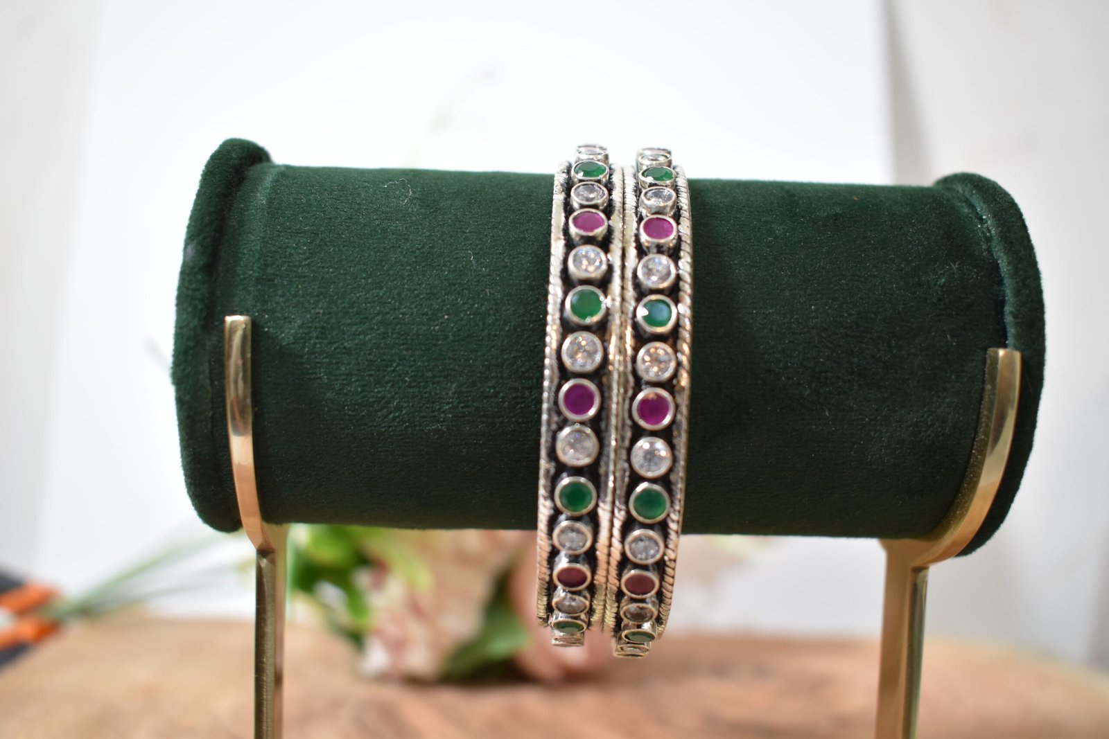 round-green-white-ruby-colour-cutstone-sequence-silver-kada.4 A pair of 925 sterling silver kadas standing upright against a soft gradient background, featuring a continuous sequence of round green, clear white, and ruby red cut stones bordered by textured silver detailing.