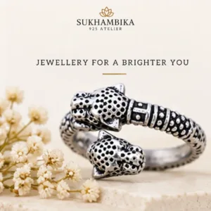 Promotional product image of the classic lion face chitai silver band resting on a stone block with delicate white flowers, featuring the text "Sukhambika 925 Atelier Jewellery for a Brighter You".
