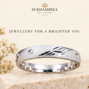 Promotional product image of the impressive silver band resting on a stone block with delicate white flowers, featuring the text "Sukhambika 925 Atelier Jewellery for a Brighter You".