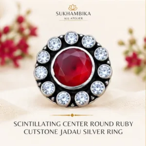 Promotional product image of the ruby jadau silver ring resting on a stone block with delicate white flowers, featuring the text "Sukhambika 925 Atelier Jewellery for a Brighter You".
