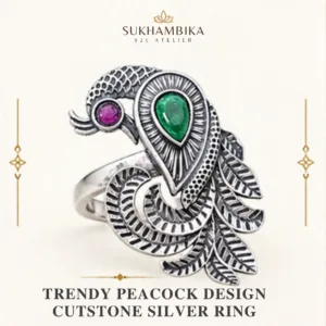 Main promotional product image of the trendy peacock design cutstone silver ring resting on a white surface, clearly showing the green and magenta stones and oxidized tail feathers.